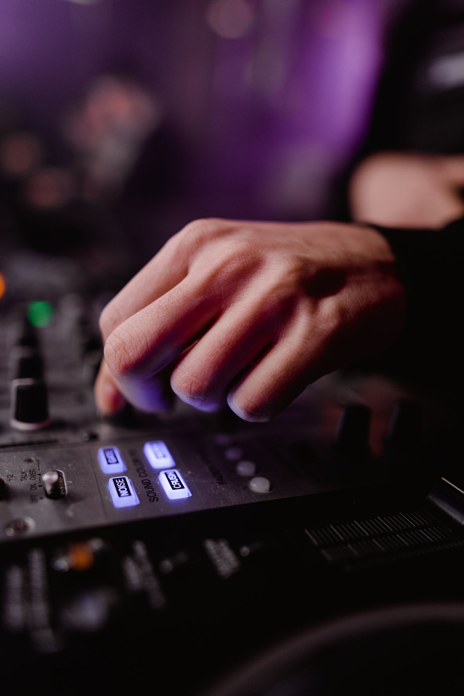 Close-up of a hand adjusting knobs and lit buttons on a DJ mixing console under purple lighting